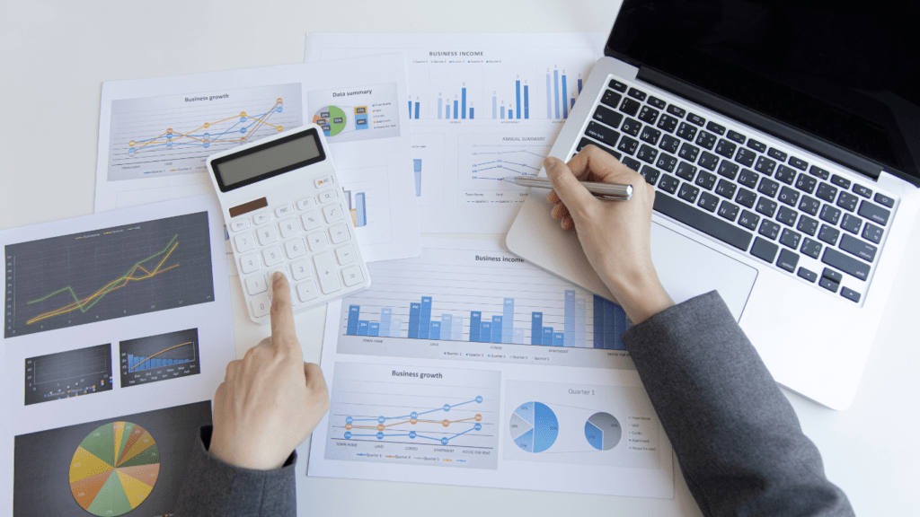 a person is using a calculator and a laptop on a desk with graphs and papers