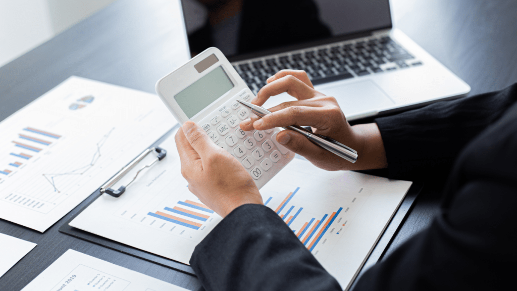 a person is using a calculator and a laptop on a desk with graphs and papers