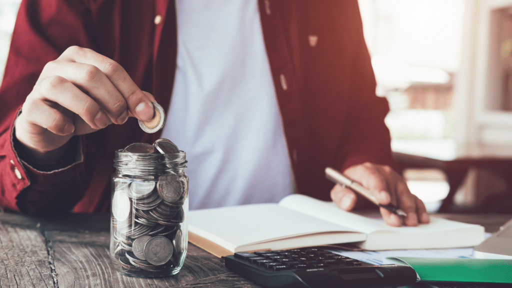 a person putting coins in a jar on a desk