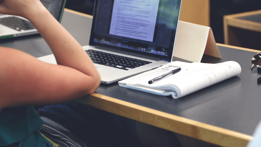 a person sitting at a desk with two laptops and a computer screen